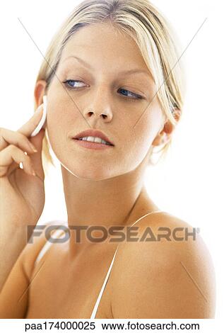 Stock Photography - Young woman pressing cotton pad to face, looking out of corner of eyes, head and shoulders. Fotosearch