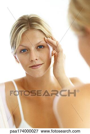 Stock Photo - Young woman reflected in mirror, looking in camera, head and shoulders. Fotosearch