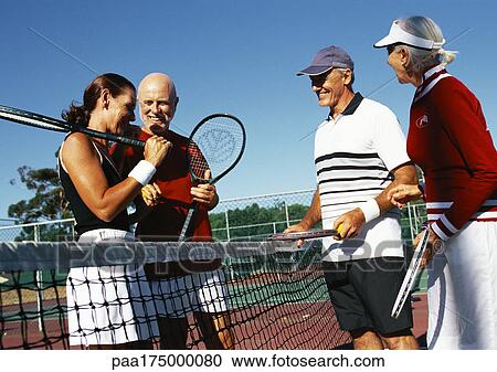 Stock Image - Four mature tennis players on court, side view. Fotosearch