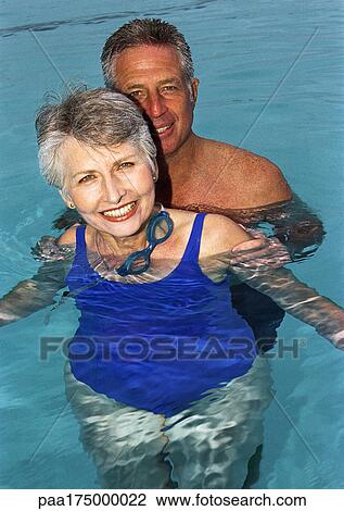 Stock Image - Mature couple in swimming pool, smiling, portrait. Fotosearch