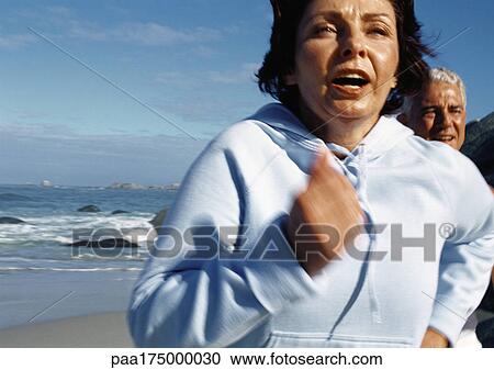 Stock Image - Mature couple running on beach, close-up. Fotosearch