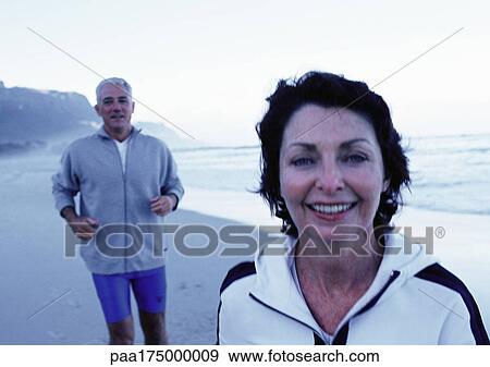 Stock Photo - Mature man and woman in sportswear on beach. Fotosearch