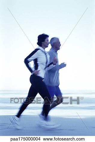 Picture - Mature man and woman running on beach, side view. Fotosearch