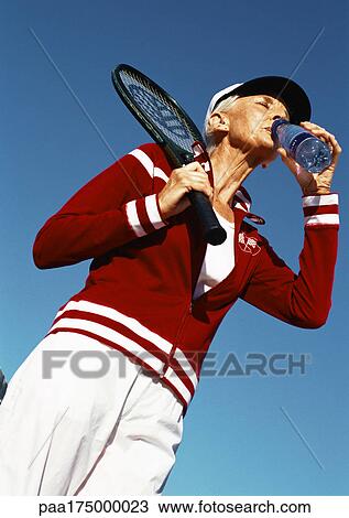 Mature woman holding tennis racket and drinking from bottle of water, low angle view View Large Photo Image Stock Image - Mature woman holding tennis racket and drinking from bottle of water, low angle view. Fotosearch