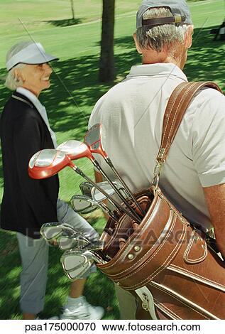 Stock Image - Two mature golfers, one carrying clubs, rear view. Fotosearch