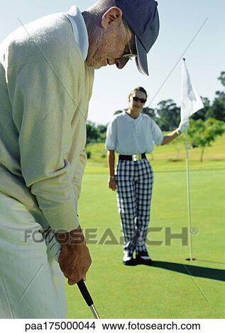Two mature golfers playing, one putting, the other holding flag View Large Photo Image Picture - Two mature golfers playing, one putting, the other holding flag. Fotosearch
