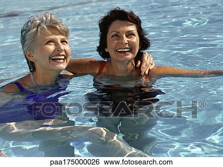 Stock Photograph - Two mature women in swimming pool, smiling. Fotosearch