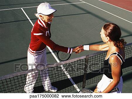 Stock Image - Two mature women shaking hands on tennis court. Fotosearch