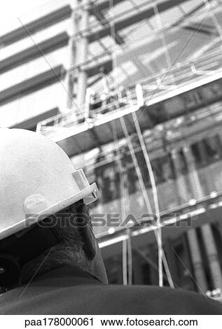 Stock Image - Builder looking at scaffolding, rear view, close-up, b&w. Fotosearch