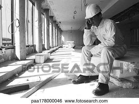 Stock Photograph - Builder sitting with cell phone, b&w. Fotosearch