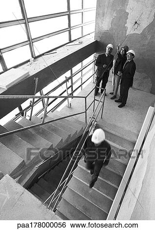 Stock Photograph - Four people on stairs, wearing hard hats, b&w. Fotosearch