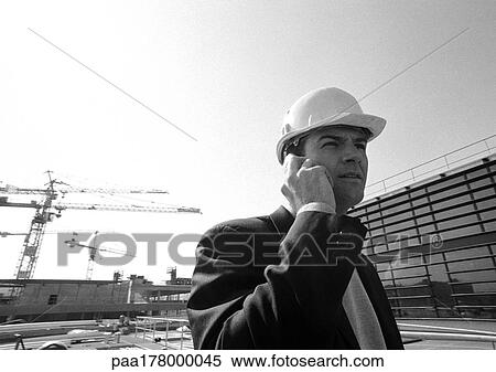 Man in hard hat using cell phone, close-up, in front of construction sight, b&w View Large Photo Image Stock Photography - Man in hard hat using cell phone, close-up, in front of construction sight, b&w. Fotosearch
