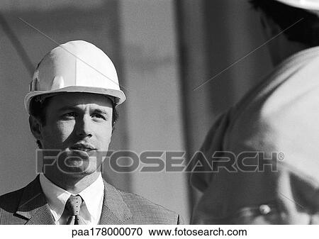 Stock Image - Man in suit wearing hard hat, close-up, b&w. Fotosearch