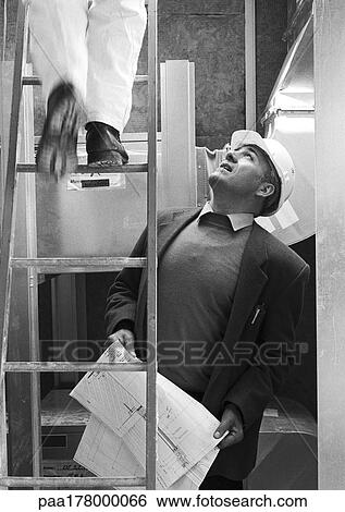 Man with hard hat looking at man on stepladder, b&w View Large Photo Image Stock Photograph - Man with hard hat looking at man on stepladder, b&w. Fotosearch