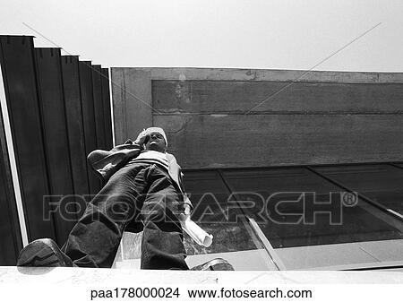 Man with hard hat using cell phone, low angle view, b&w View Large Photo Image Picture - Man with hard hat using cell phone, low angle view, b&w. Fotosearch