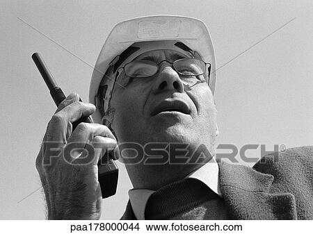 Man with hard hat using walkie-talkie, close-up, low angle view, b&w View Large Photo Image Picture - Man with hard hat using walkie-talkie, close-up, low angle view, b&w. Fotosearch
