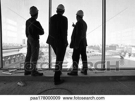 Three men wearing hard hats, looking out of window, rear view, b&w View Large Photo Image Stock Photo - Three men wearing hard hats, looking out of window, rear view, b&w. Fotosearch