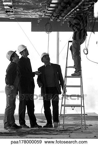 Three men with hard hats looking at man on stepladder, b&w View Large Photo Image Stock Photo - Three men with hard hats looking at man on stepladder, b&w. Fotosearch
