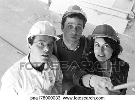Stock Image - Two men and woman wearing hard hats, elevated view, b&w. Fotosearch