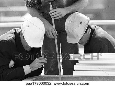 Stock Image - Two men wearing hard hats, man holding folding ruler, b&w. Fotosearch