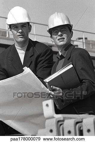 Two men with hard hats holding blueprints, b&w View Large Photo Image Stock Photo - Two men with hard hats holding blueprints, b&w. Fotosearch