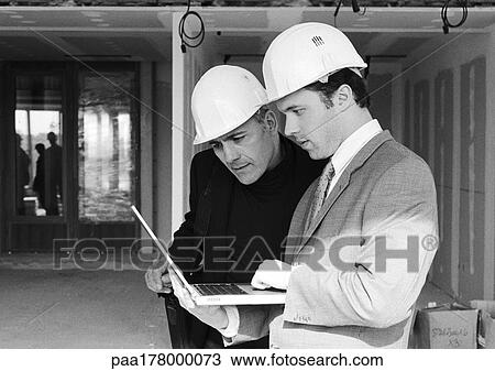 Two men with hard hats, one holding laptop computer, b&w View Large Photo Image Stock Image - Two men with hard hats, one holding laptop computer, b&w. Fotosearch