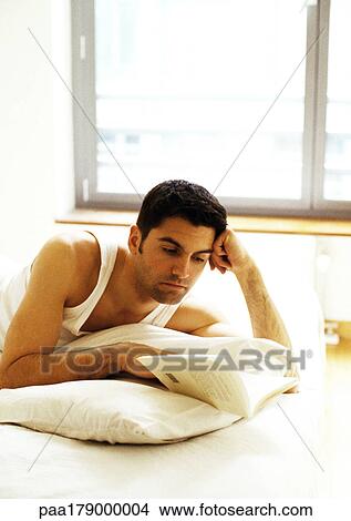 Picture - Man lying on bed, reading book. Fotosearch