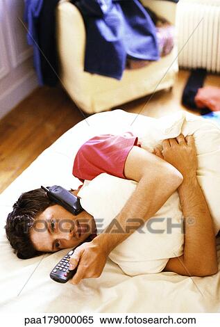 Man lying on bed with phone and remote control View Large Photo Image Stock Photography - Man lying on bed with phone and remote control. Fotosearch
