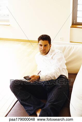 Man lying on sofa with remote control View Large Photo Image Stock Photo - Man lying on sofa with remote control. Fotosearch