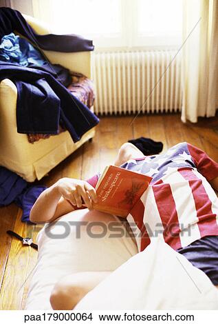 Picture - Man resting on bed with book in hand. Fotosearch