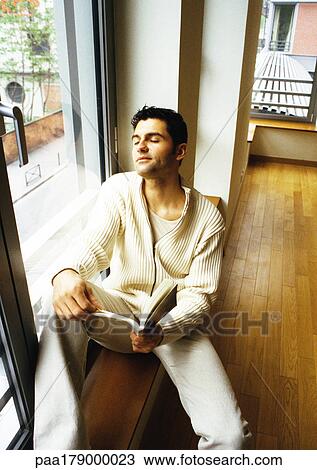 Man sitting near window with book View Large Photo Image Stock Image - Man sitting near window with book. Fotosearch