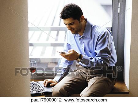Man sitting with laptop computer and glass of wine, using cell phone View Large Photo Image Stock Image - Man sitting with laptop computer and glass of wine, using cell phone. Fotosearch