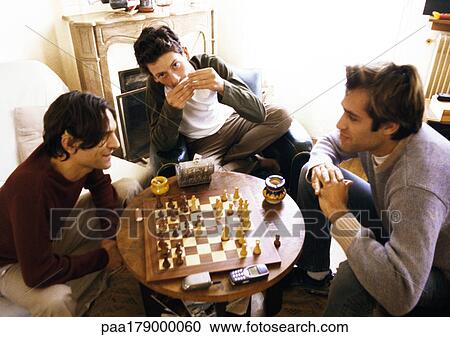 Three men in living room, two playing chess View Large Photo Image Stock Image - Three men in living room, two playing chess. Fotosearch