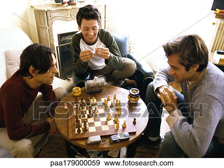 Three men in living room, two playing chess View Large Photo Image Stock Photo - Three men in living room, two playing chess. Fotosearch