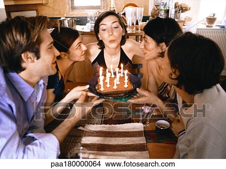 Four people holding cake, woman blowing out candles View Large Photo Image Picture - Four people holding cake, woman blowing out candles. Fotosearch
