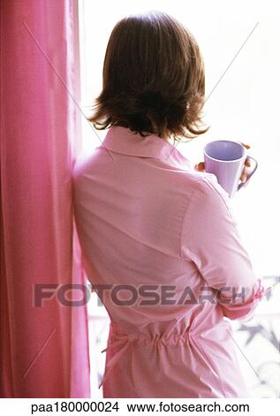 Woman holding mug, looking out window, rear view View Large Photo Image Picture - Woman holding mug, looking out window, rear view. Fotosearch