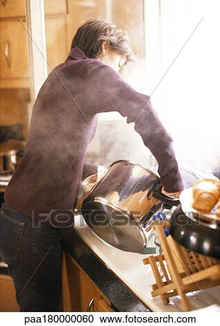 Woman holding steaming pot above sink View Large Photo Image Stock Image - Woman holding steaming pot above sink. Fotosearch