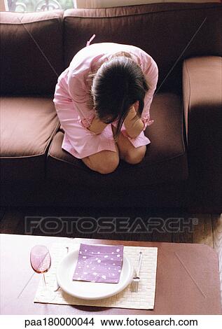 Picture - Woman kneeling on sofa, head in hands. Fotosearch