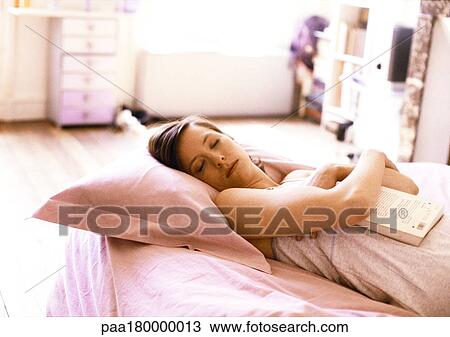Stock Image - Woman lying in bed, holding book with eyes closed. Fotosearch