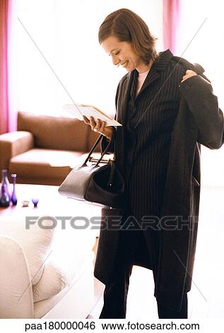 Woman putting coat on while reading View Large Photo Image Stock Photograph - Woman putting coat on while reading. Fotosearch