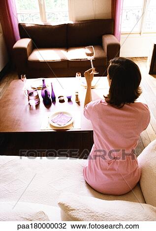Woman sitting in living room, holding up wine glass, rear view View Large Photo Image Stock Image - Woman sitting in living room, holding up wine glass, rear view. Fotosearch