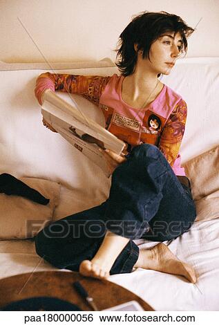 Stock Photograph - Woman sitting on sofa, holding newspaper, looking away. Fotosearch