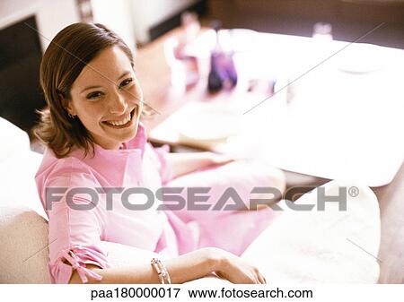 Woman sitting on sofa, smiling, portrait View Large Photo Image Stock Photo - Woman sitting on sofa, smiling, portrait. Fotosearch
