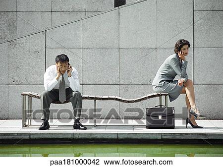 Businessman and woman on bench, using cell phones View Large Photo Image Stock Image - Businessman and woman on bench, using cell phones. Fotosearch