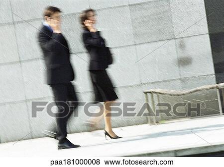 Stock Photo - Businessman and woman using cell phones in street, full length, blurred motion. Fotosearch