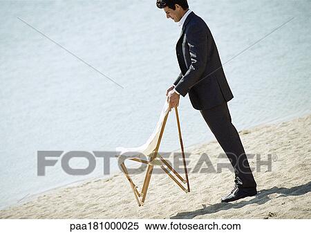 Businessman holding chair on beach View Large Photo Image Stock Photography - Businessman holding chair on beach. Fotosearch