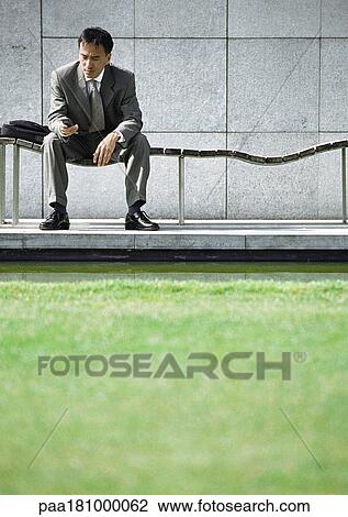Businessman on bench looking at cell phone View Large Photo Image Stock Image - Businessman on bench looking at cell phone. Fotosearch