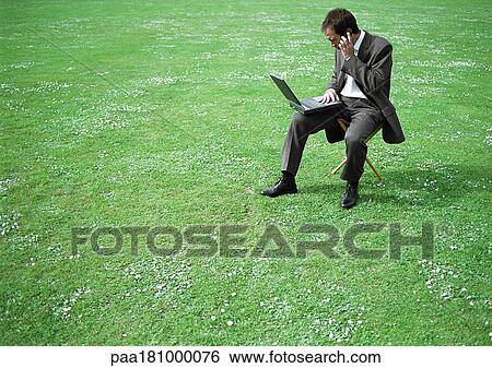 Businessman sitting on chair in grassy field with laptop and cell phone View Large Photo Image Stock Photograph - Businessman sitting on chair in grassy field with laptop and cell phone. Fotosearch