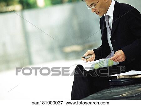 Businessman sitting outdoors, examining documents View Large Photo Image Stock Photo - Businessman sitting outdoors, examining documents. Fotosearch