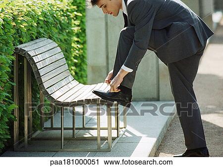 Stock Image - Businessman tying shoelaces on bench. Fotosearch